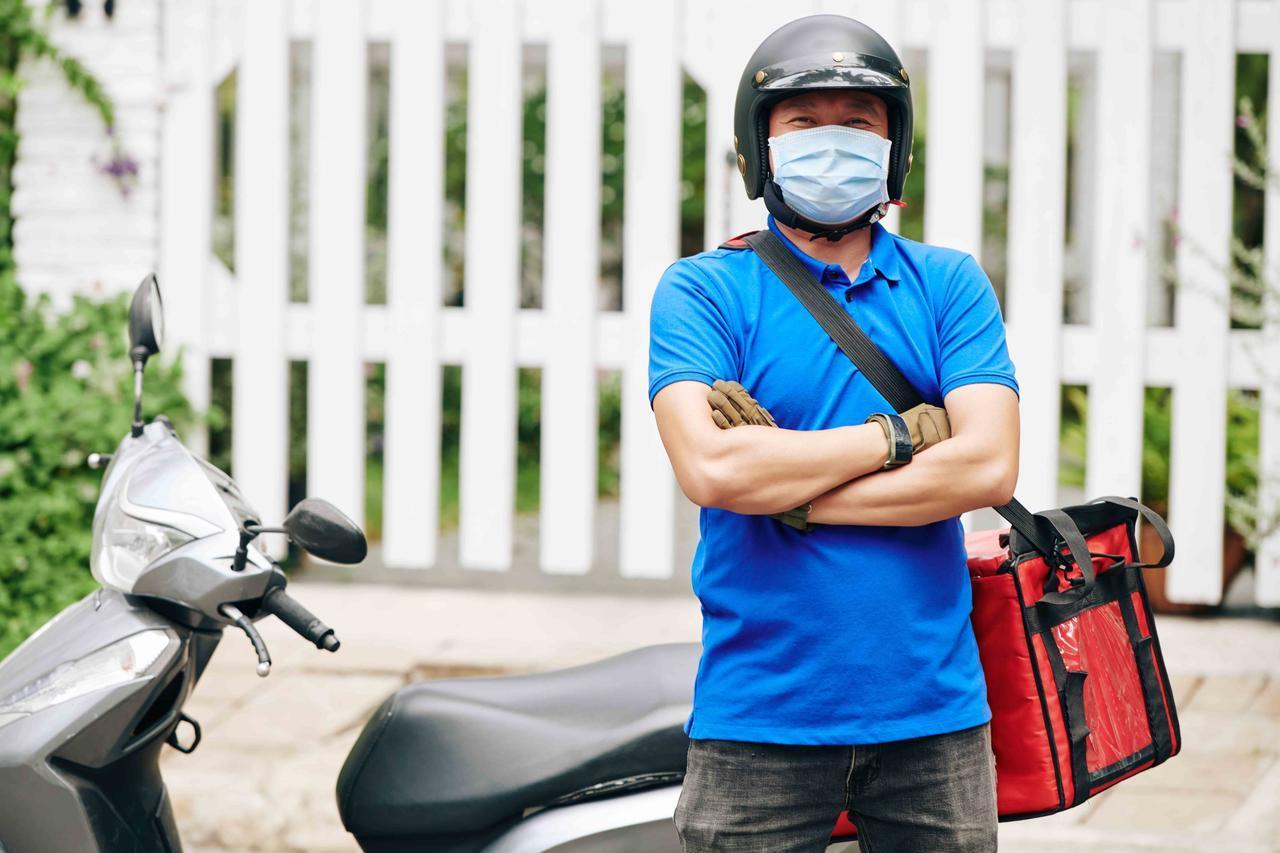 Portrait of happy confident delivery man standing at scooter with big cooler bag full of products